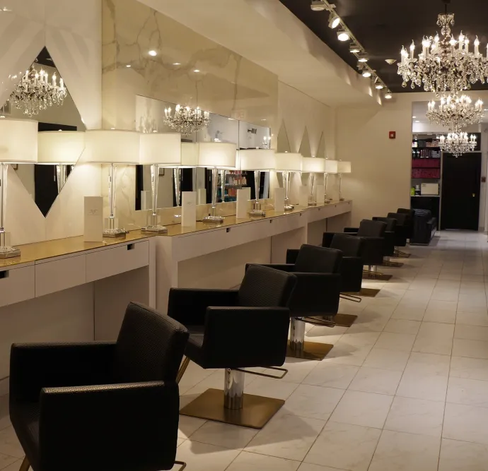 Salon with a row of styling stations, chandeliers, and mirrors.