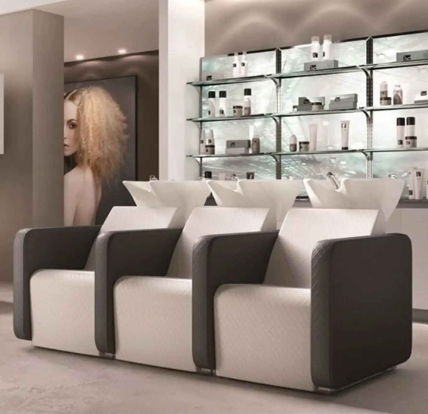 Upscale hair salon with three connected shampoo chairs in dark charcoal and quilted cream upholstery, white ceramic wash bowls, and backlit glass shelving with professional hair products